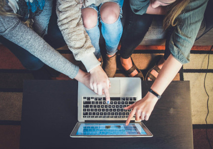 
                            
                            Three women pointing their index fingers at a laptop screen
                            
                            